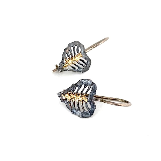 Boucles crochets façonnées en argent patiné, elles présentent un travail d'ajourage grâce à un ciselage. Au centre, une nervure centrale est soulignée d'une touche d'or jaune.