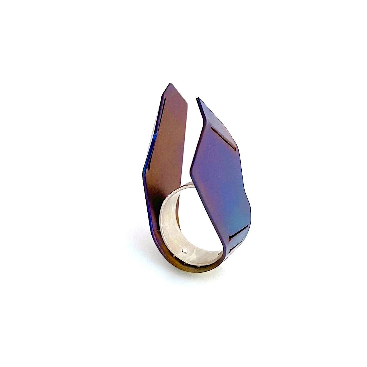 Cette bague asymétrique, toute en hateur aux formes aériennes est construite comme deux ailes verticales, à partir d'une plaque de titane pliée, sciée, et rivetée à un anneau d'argent. La surface du métal est chauffé à la flamme pour un rendu bleu vif aux nuances brun, violet.