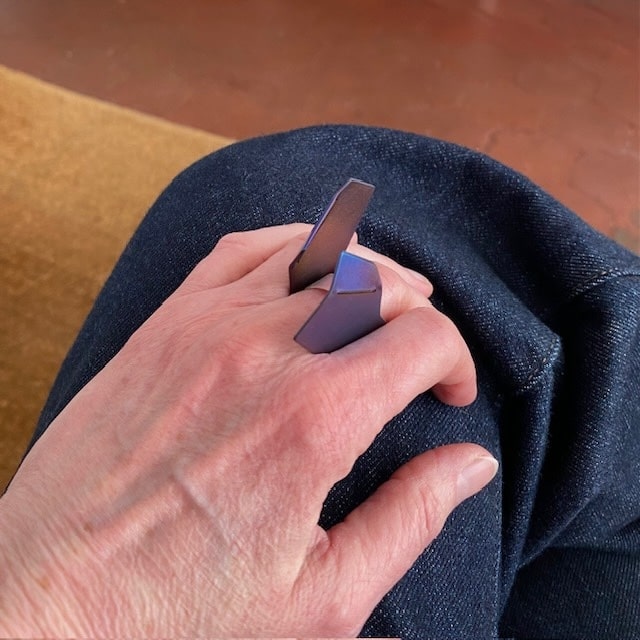 Bague asymétrique et sculptural en forme de deux ailes verticales. Le titane est plié et scié puis riveté à un anneau en argent brossé. Le métal est chauffé à la flamme pour obtenir une patine bleue vive aux reflets brun, violet. Bijou porté.