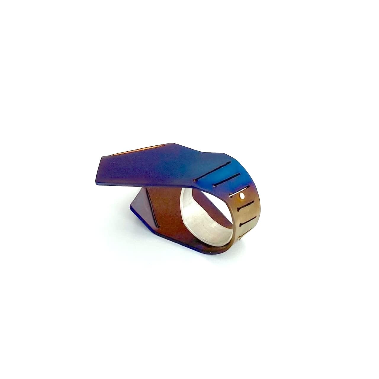 Cette bague asymétrique aux formes aériennes est construite comme deux ailes verticales, à partir d'une plaque de titane pliée, sciée, puis rivetée à un anneau d'argent. La surface du métal est chauffé à la flamme pour un rendu bleu vif aux nuances brun, violet.
