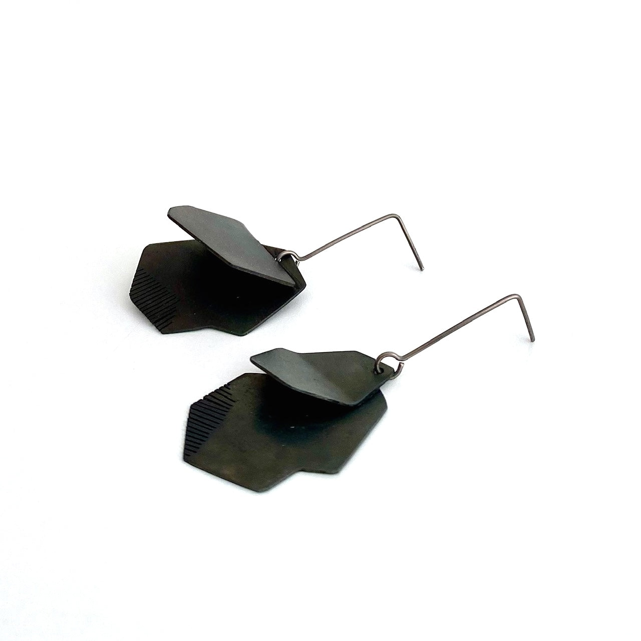 Boucles pendantes architecturales en acier patiné noir, plié et scié par endroit en lamelles. Elles sont montées sur des tiges droites en titane.