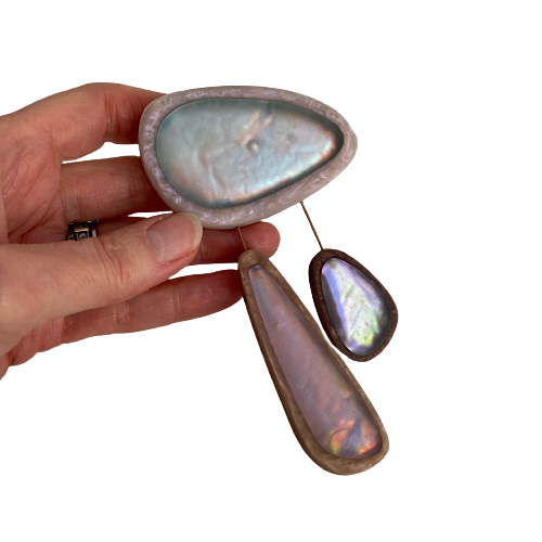 broche composée de 3 éléments de différentes tailles en résine couleurs pastel bleu clair,rose,bleu. les deux petits éléments sont reliés au grand par un cable rigide noir. fermeture aimant.broche tenue par main de femme