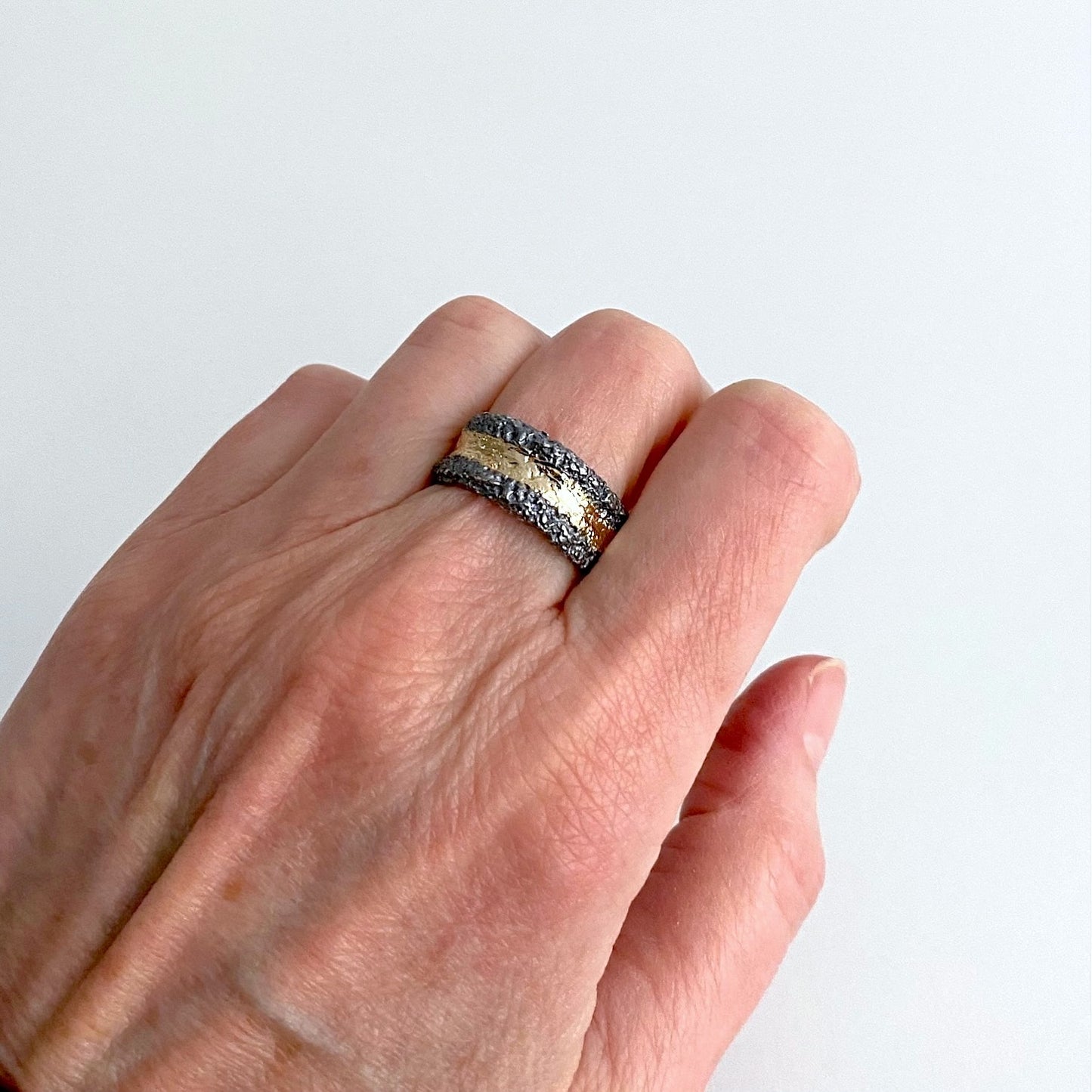 Anneau large en argent patiné noir. et texturé. Sur le dessus un bande d'or jaune est appliquée sur la moitié du bijou. Bague portée.