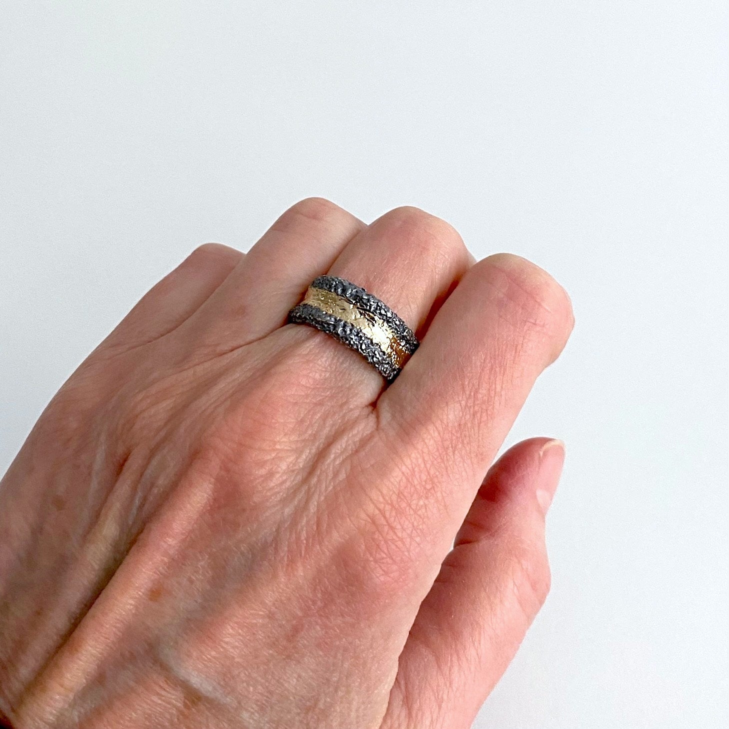 Anneau large en argent patiné noir. et texturé. Sur le dessus un bande d'or jaune est appliquée sur la moitié du bijou. Bague portée.