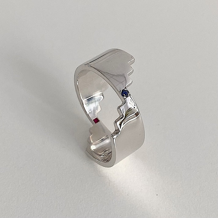 Anneau large en argent rhodié, marqué d'une découpe en escalier. Cette bague réversible offre deux facettes distinctes, chacune sublimée par un saphir bleu ou rose.