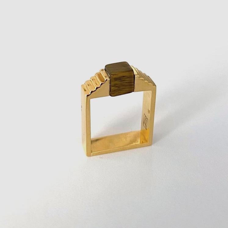 Bague géométrique en vermeil avec une pierre oeil de tigre en forme de cube, imbriqué entre deux éléments en formes d'escalier.