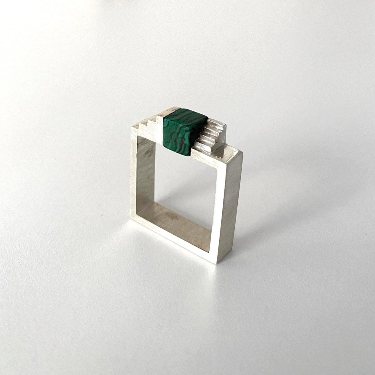 Bague carrée en argent brossé, au centre un cube de malachite est enchâssé entre deux éléments inversés en forme d'escalier.