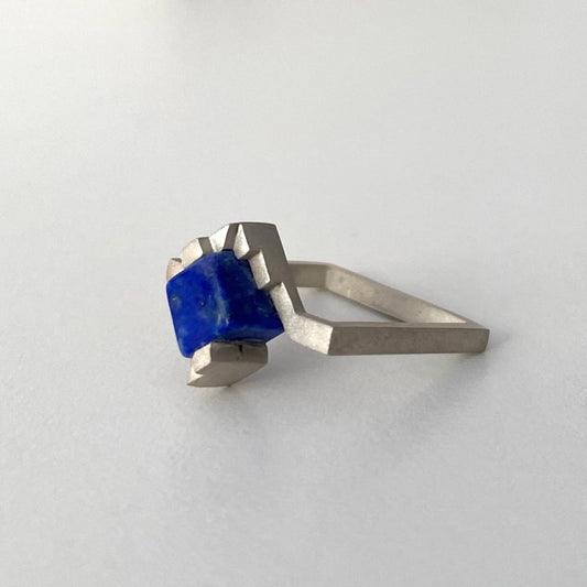 Solitaire, anneau fin et carré en argent brossé avec un cube de lapis-lazuli imbriqué entre deux éléments en formes d'escalier.