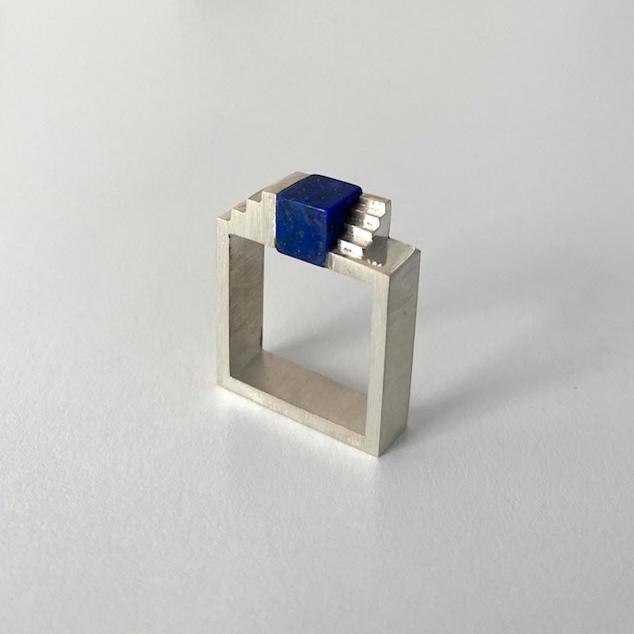 Bague carrée en argent brossé, au centre un cube de lapis-lazuli est enchâssé entre deux éléments inversés en forme d'escalier.