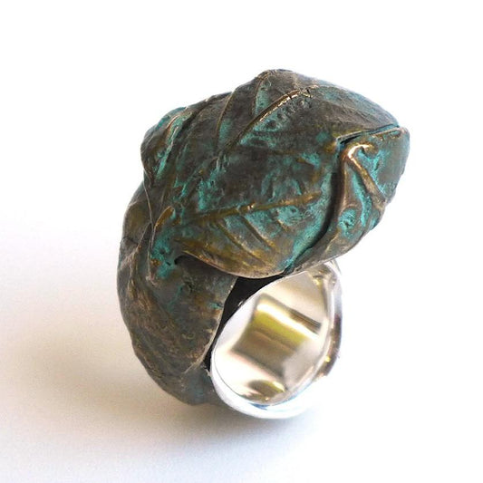  Bague sculpturale évoquant l'éveille de la nature avec une feuille d'arbre délicatement recroquevillée sur le doigt, comme un cocon végétal. Réalisée en bronze patiné au vert-de-gris, elle se distingue par ses nuances organiques. 