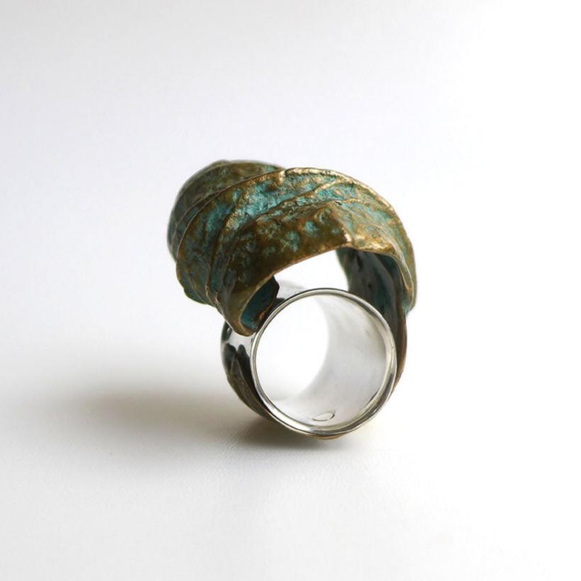 Bague sculpturale évoquant la nature avec une feuille d'arbre finement enroulée autour du doigt, comme une étreinte végétale. Réalisée en bronze patiné au vert-de-gris. Vue de face sur fond blanc.