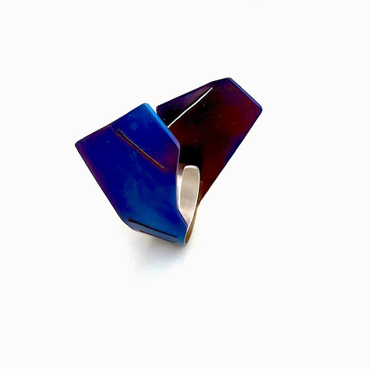 Bague aux formes aériennes est construite comme une sculpture, à partir d'une plaque de titane pliée, finement sciée, puis rivetée à un anneau d'argent à la forme géométrique. La surface du métal est chauffé à la flamme pour un rendu bleu vif aux nuances brun, violet.