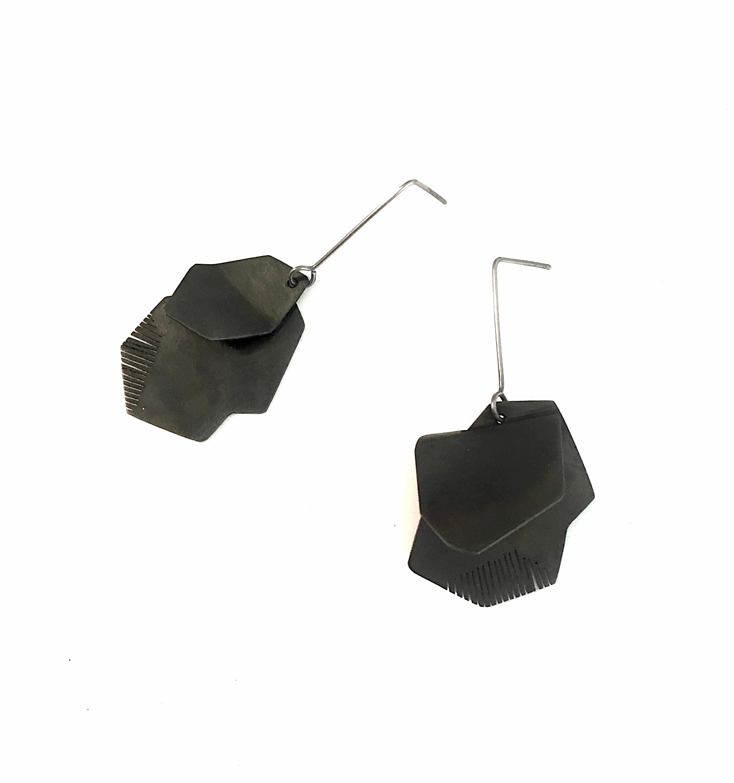 Boucles pendantes architecturales en acier patiné noir, plié et scié par endroit en lamelles. Elles sont montées sur des tiges droites en titane.
