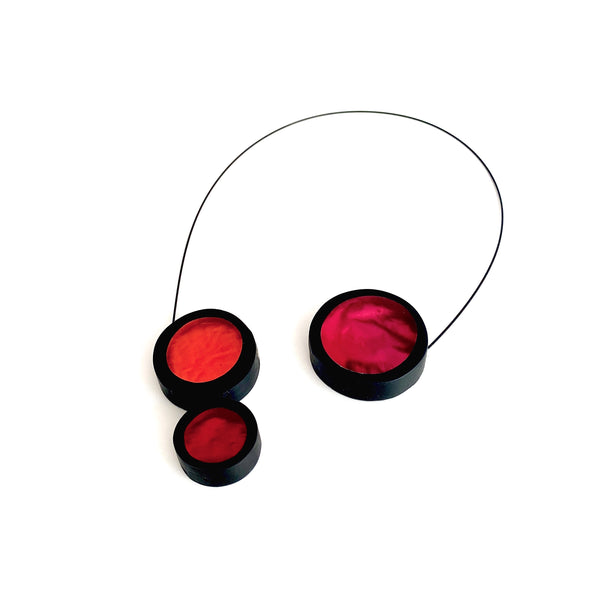 Collier 3 ronds de résine couleurs rouge, orange et fushia assemblés sur un câble noir aimanté. Collier ouvert.