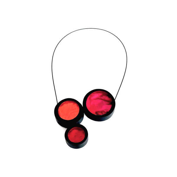 Collier 3 ronds de résine couleurs rouge, orange et fushia assemblés sur un câble noir aimanté. vue de face.