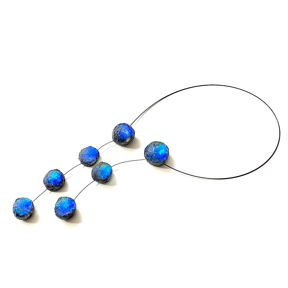 Ce collier en forme de cravate est composé de 7 sphères en résine aux nuances de bleu, assemblées sur un cable noir. Ce bijou asymétrique et texturé est léger et confortable, il offre une fermeture discrète et résistante grâce à un fermoir aimanté intégré dans deux éléments de résine.