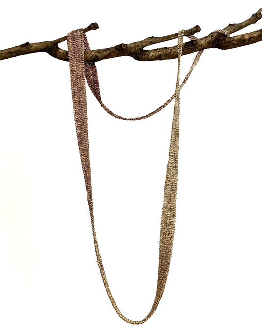 Long collier mordoré, en forme de ruban dégradé composé de chaîne d'argent patiné et fil de soie. Bijou présenté sur une branche d'arbre.