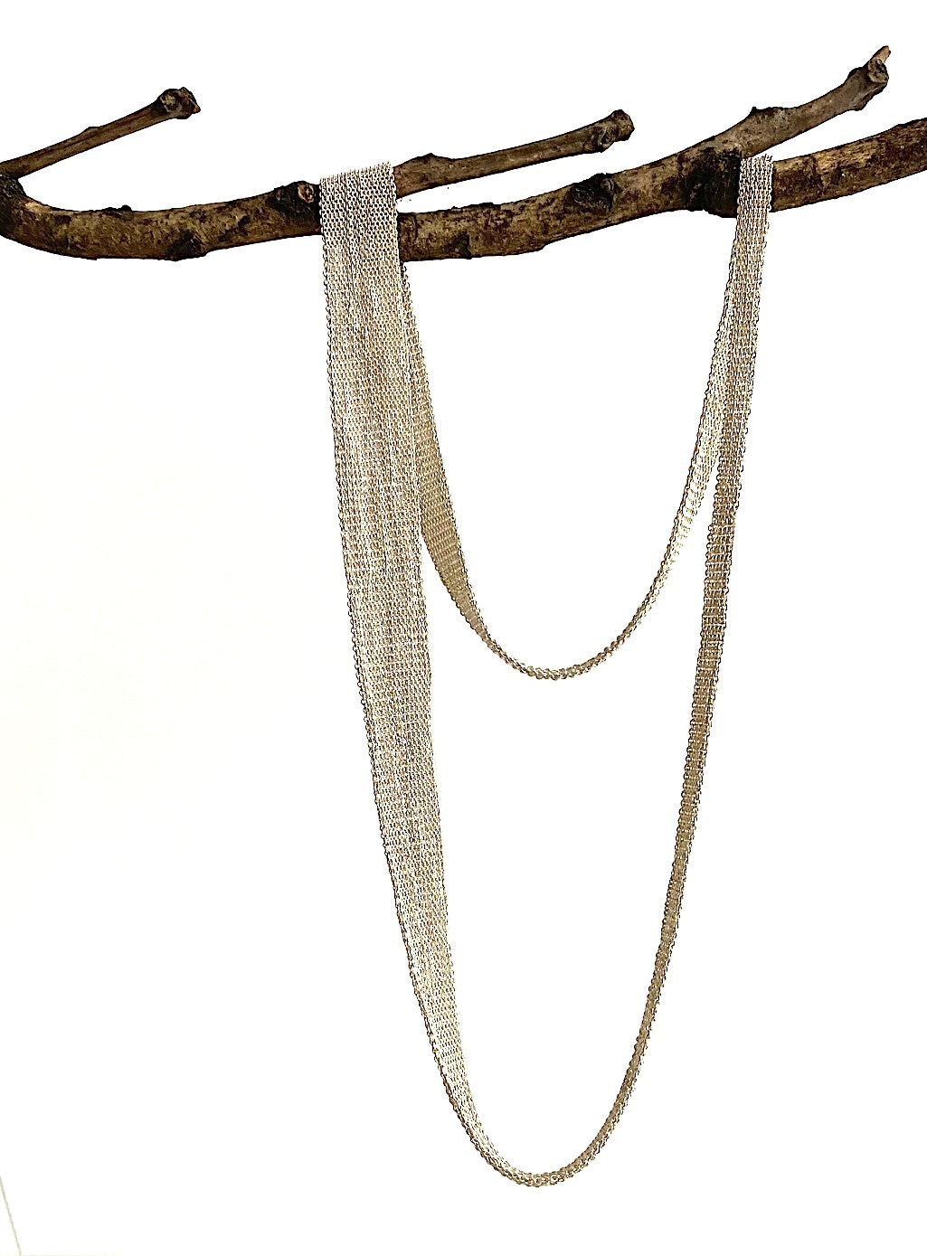 Long collier, composé de chaîne d'argent et fil de soie en forme de ruban dégradé. Bijou présenté sur une branche d'arbre.