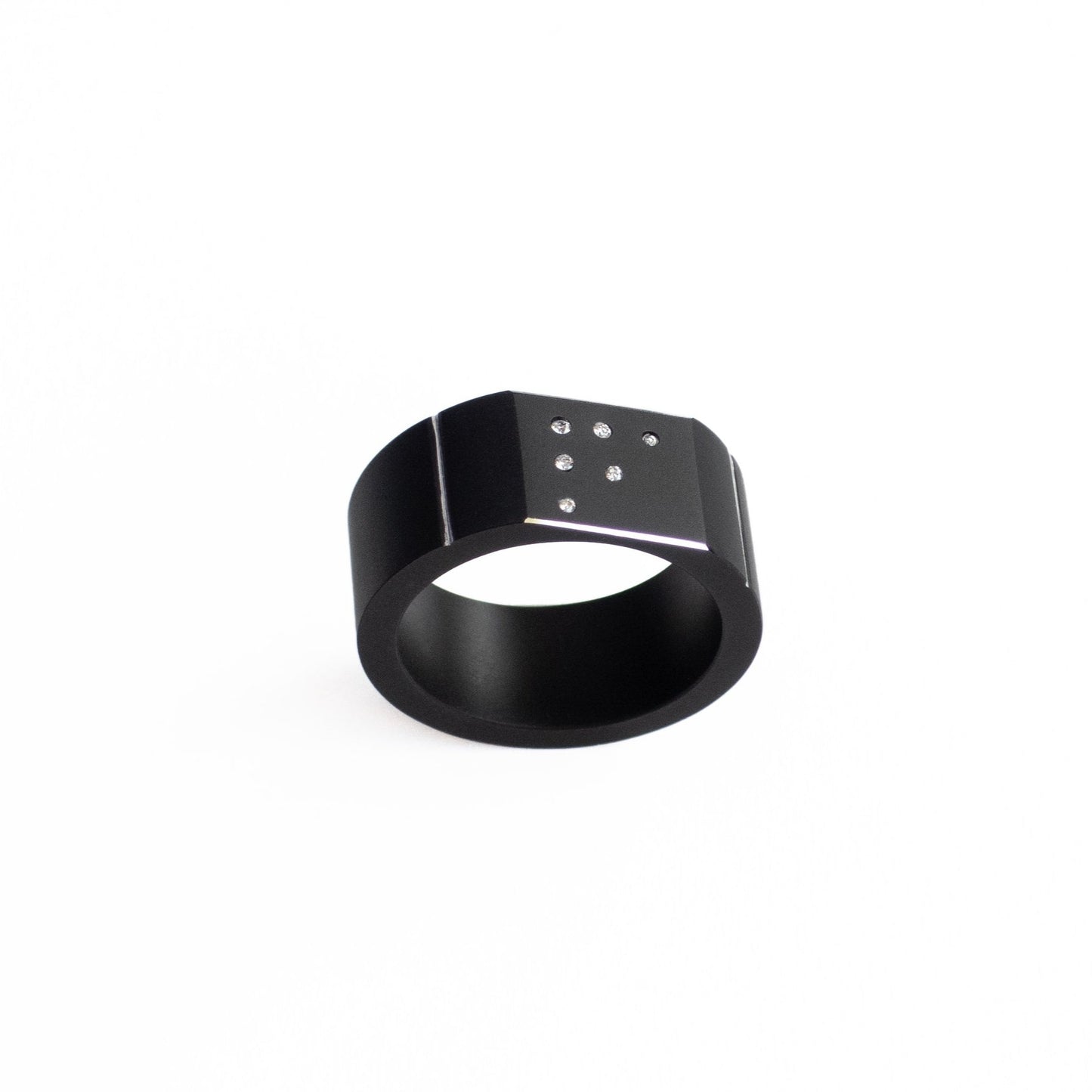 Bague moderne forme chevalière en aluminium anodisé noir mat, fini par trois filets polis miroir. Sur la surface plane du bijou, six petits diamants blancs sont sertis en dégradé. vue de profil.