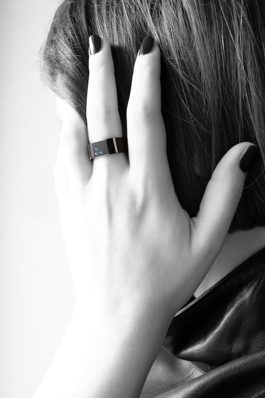 Bague chevalière en aluminium anodisé noir ornée de trois apatites en dégradé est présentée sur une main de femme.