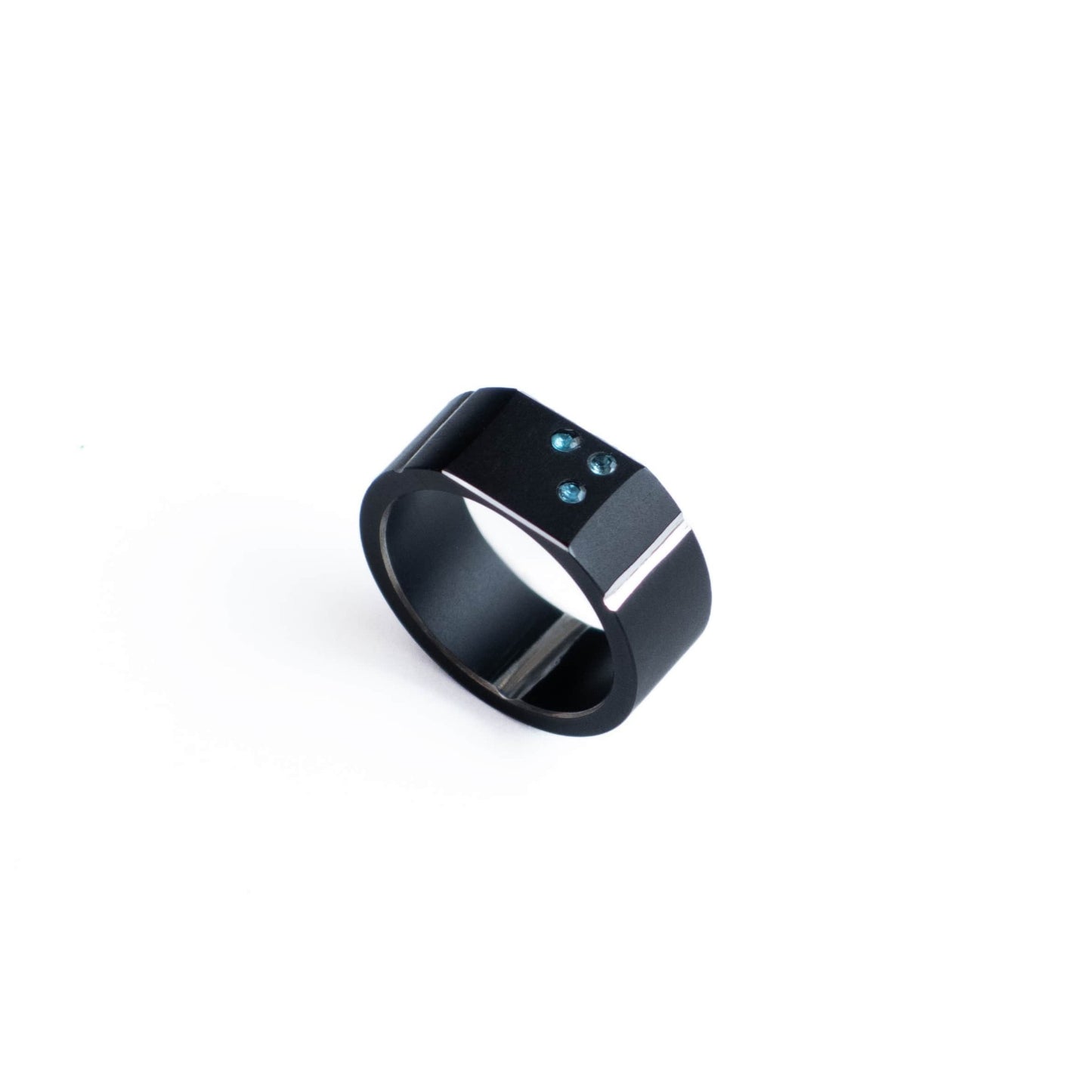 Bague forme chevalière en aluminium anodisé noir ornée des trois apatites bleu vif sur le dessus plane du bijou. Ce modèle est fini par deux filets polis miroir.