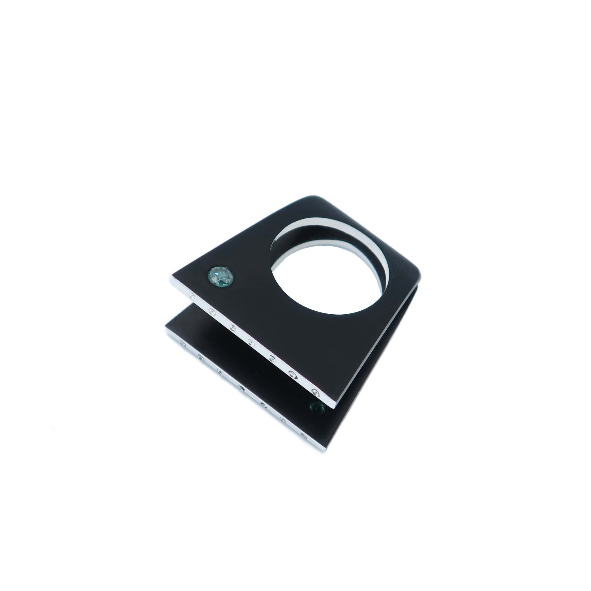 Bague design à deux faces en aluminium noir serties chacune d'un diamant bleu-vert. Sur le dessus deux lignes polies sont serties de sept petits diamants blancs chacune. Bague à plat sur fond blanc.