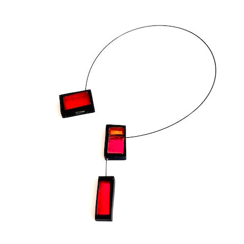 Collier ouvert avec 3 rectangles de résine rouge, orange et rose assemblés sur un câble noir. Fermoir aimant inséré dans la résine.&nbsp;