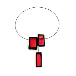 Collier avec trois rectangles de résine rouge, orange et rose assemblés sur un câble noir aimanté. Vue de face. 