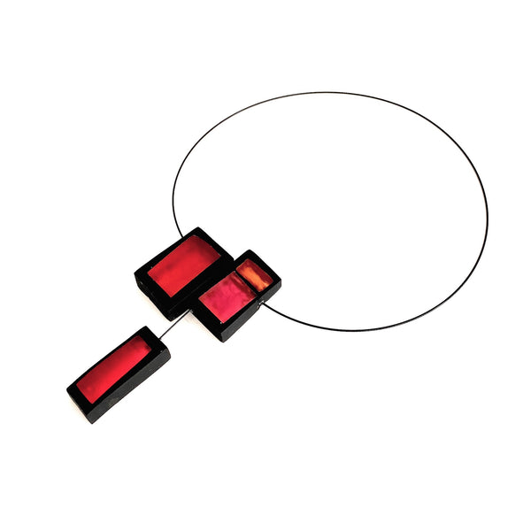 Collier avec trois rectangles de résine rouge, orange et rose assemblés sur un câble noir aimanté. Vue de profil.