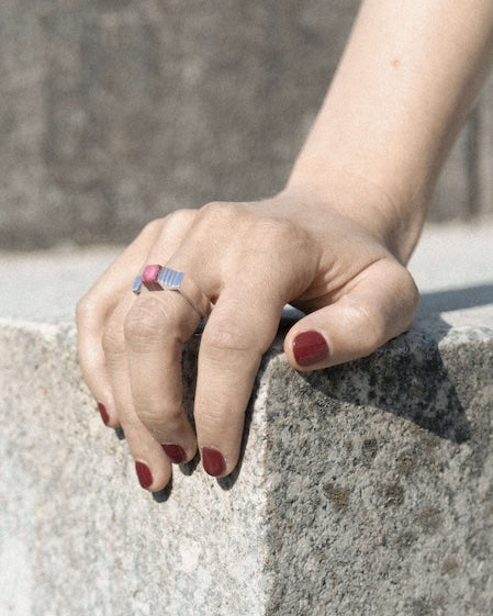 Bague carrée en argent avec un cube de corail imbriqué entre deux éléments en forme d'escalier. Bague portée par une femme , la main posée sur une marche d'escalier en pierre.