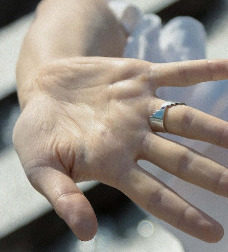 Bague géométrique et réversible présentant deux facettes distinctes, chacune sublimée par un rubis rouge. et une émeraude. Bijou porté par une main de femme.