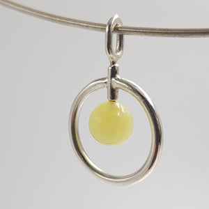 Pendentif cercle en argent forgé, au centre une perle de serpentine jaune. Bijou présenté sur cable argent.