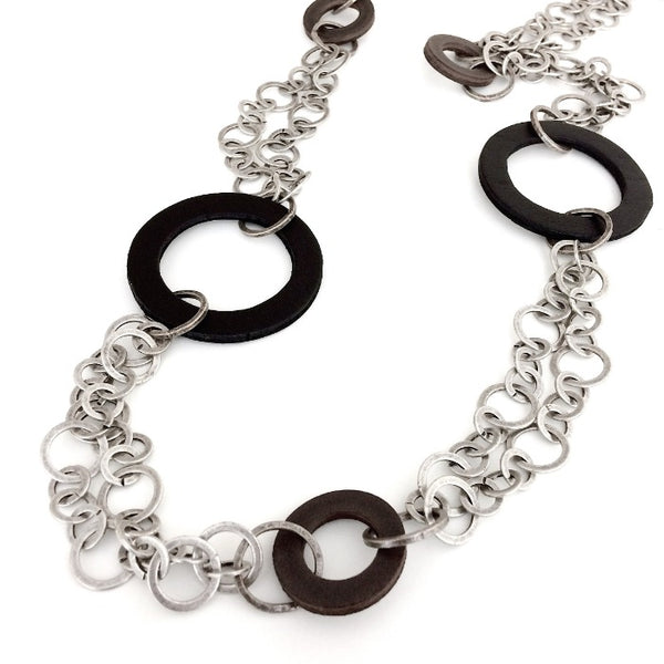 Long sautoir double chaîne métallique et cercles de cuir gris et noir de différentes tailles.