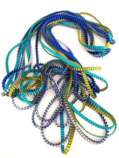 Long sautoir coloré composé de huit bandes de satin plissé bleu,silver,gold,turquoise reliées les unes aux autres par un lien de coton jaune
