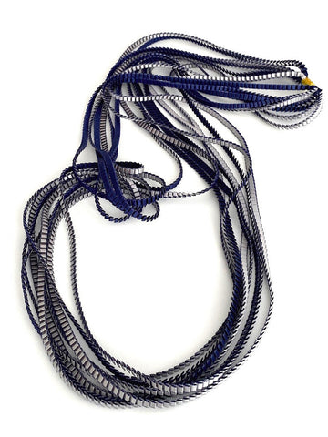 Long sautoir coloré composé de huit bandes de satin plissé bleu navy et silver reliées les unes aux autres par un lien de coton jaune.