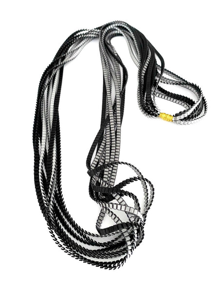 Long sautoir coloré composé de huit bandes de satin plissé noir silver reliées les unes aux autres par un lien de coton jaune