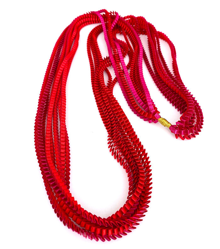 Long sautoir coloré composé de huit bandes de satin plissé rouge, fushia reliées les unes aux autres par un lien de coton jaune