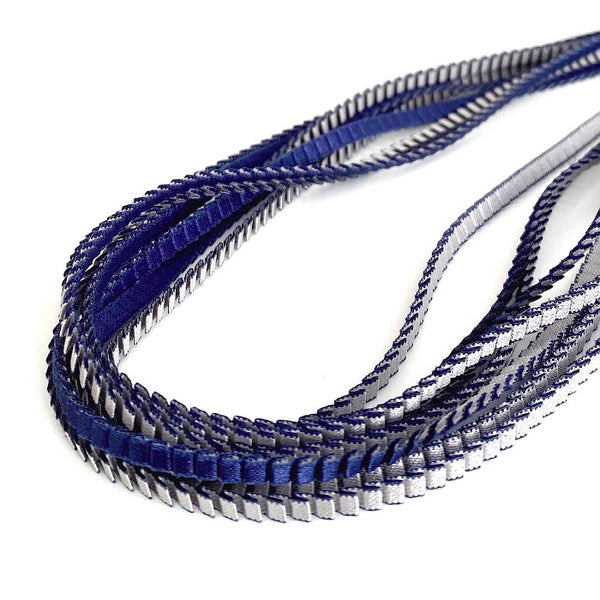 Long colli coloré composé de huit bandes de satin plissé bleu navy et silver reliées les unes aux autres par un lien de coton jaune 