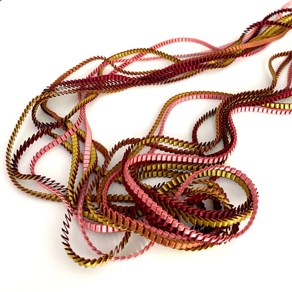 Long collier coloré composé de huit bandes de satin plissé bordeaux,marron,gold,vieux rose, pèche reliées les unes aux autres par un lien de coton jaune 