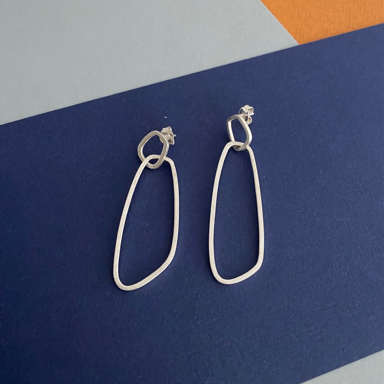 Boucles d’oreilles en argent de type mobile composées de deux pièces posées sur fond couleurs bleu, gris et jaune