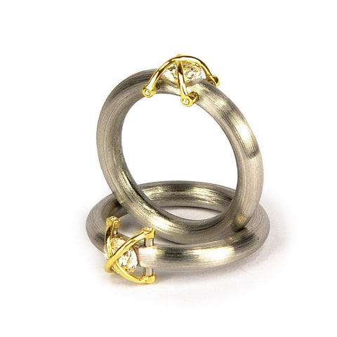 Un zircon dans une "cage" en or jaune, présenté sur un anneau en acier mat de section ronde.