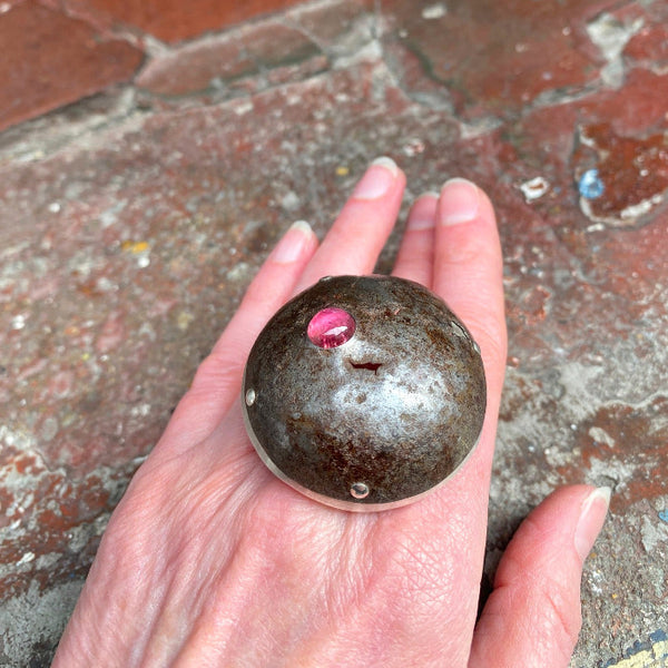 Bague en forme de dôme en fer rouillé, sur le dessus une tourmaline rose est sertie, la structure est en argent. bague sur main de femme, decor briques.