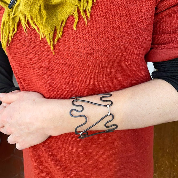 Bracelet manchette ouvert en fer martelé, porté sur un avant bras de femme