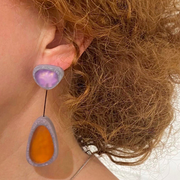 Boucles pendantes avec 2 éléments en résine orange et violet cerclé gris relié par un cable fin noir.