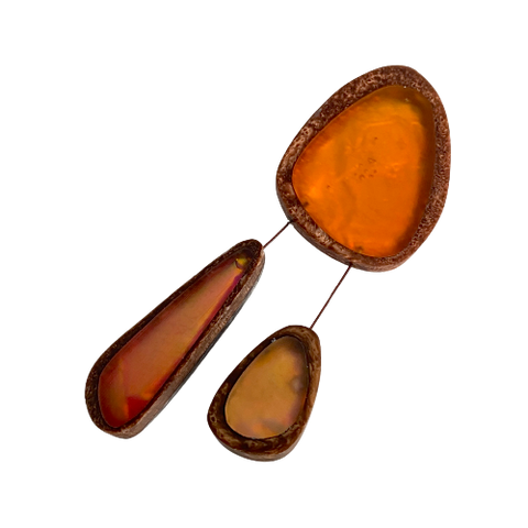 Broche en résine orange composée de trois éléments de différentes tailles,deux petits éléments sont reliés au plus grand par un cable rigide noir. fermeture aimant